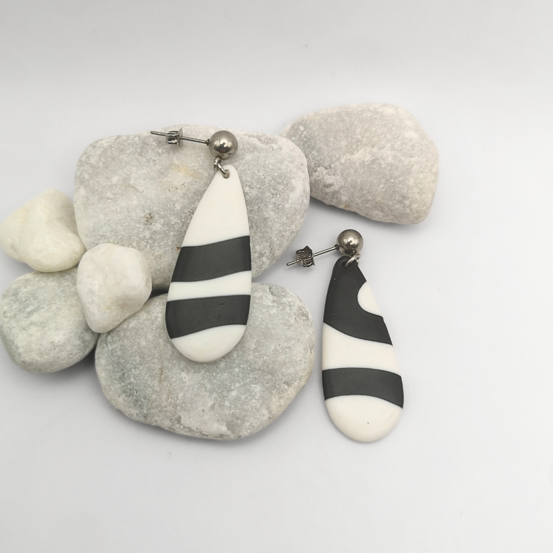 Black and white striped polymer clay earrings on a white background with pebbles.