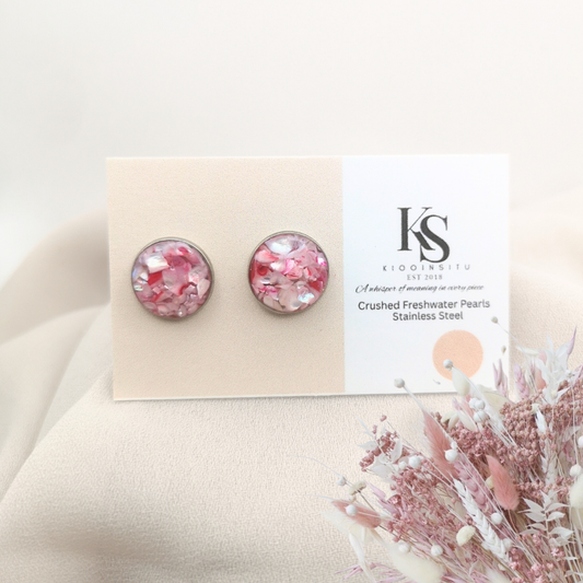 Handmade with care, these 12 mm stainless steel stud earrings feature crushed freshwater pearls in pink tones, sealed beneath a clear, glass-like resin that enhances their natural glow.