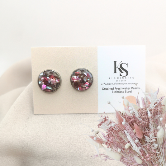 Handmade with care, these 12 mm stainless steel stud earrings feature crushed freshwater pearls in deep mocha and rose tones, sealed beneath a clear, glass-like resin.