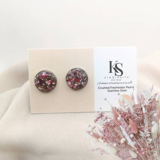 Handmade with care, these 12 mm stainless steel stud earrings feature crushed freshwater pearls in deep berry and rose tones, sealed beneath a clear, glass-like resin that enhances their natural iridescence.