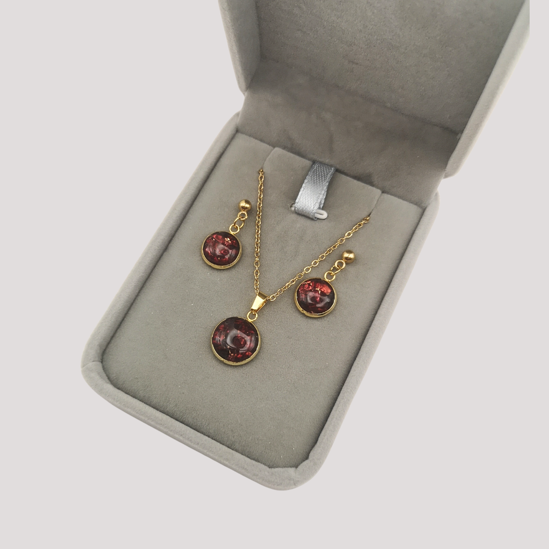 Gold jewelry set with red Garnet stones in a gray jewelry box on a light gray background