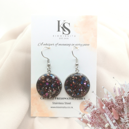 Crushed freshwater pearls shimmer in deep iridescent hues, set within 20 mm stainless steel bezels and sealed beneath a clear, glass-like resin.
