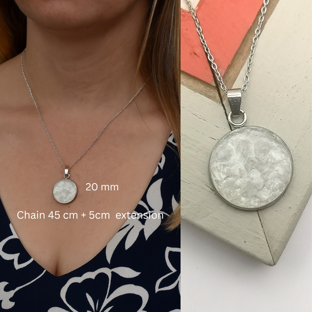Silver necklace with a round pendant worn by a person and on a stand.