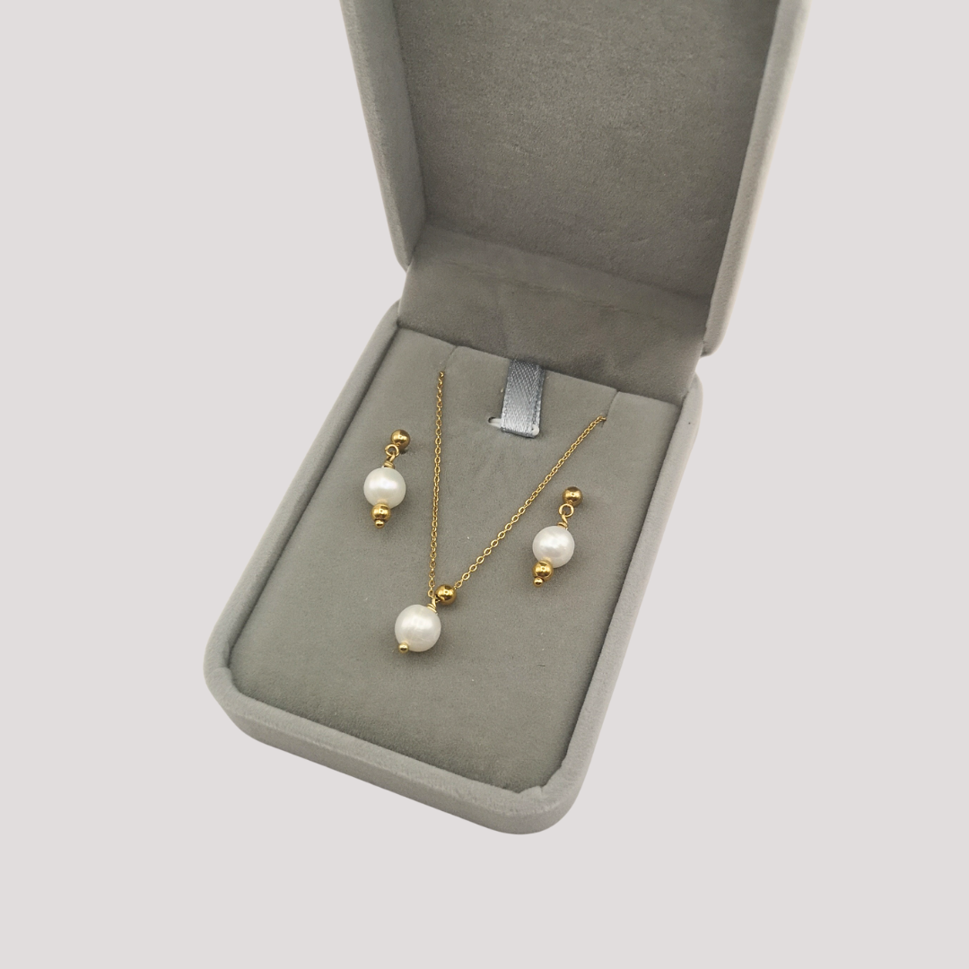 Gold necklace with pearl pendants in an open jewelry box on a light gray background