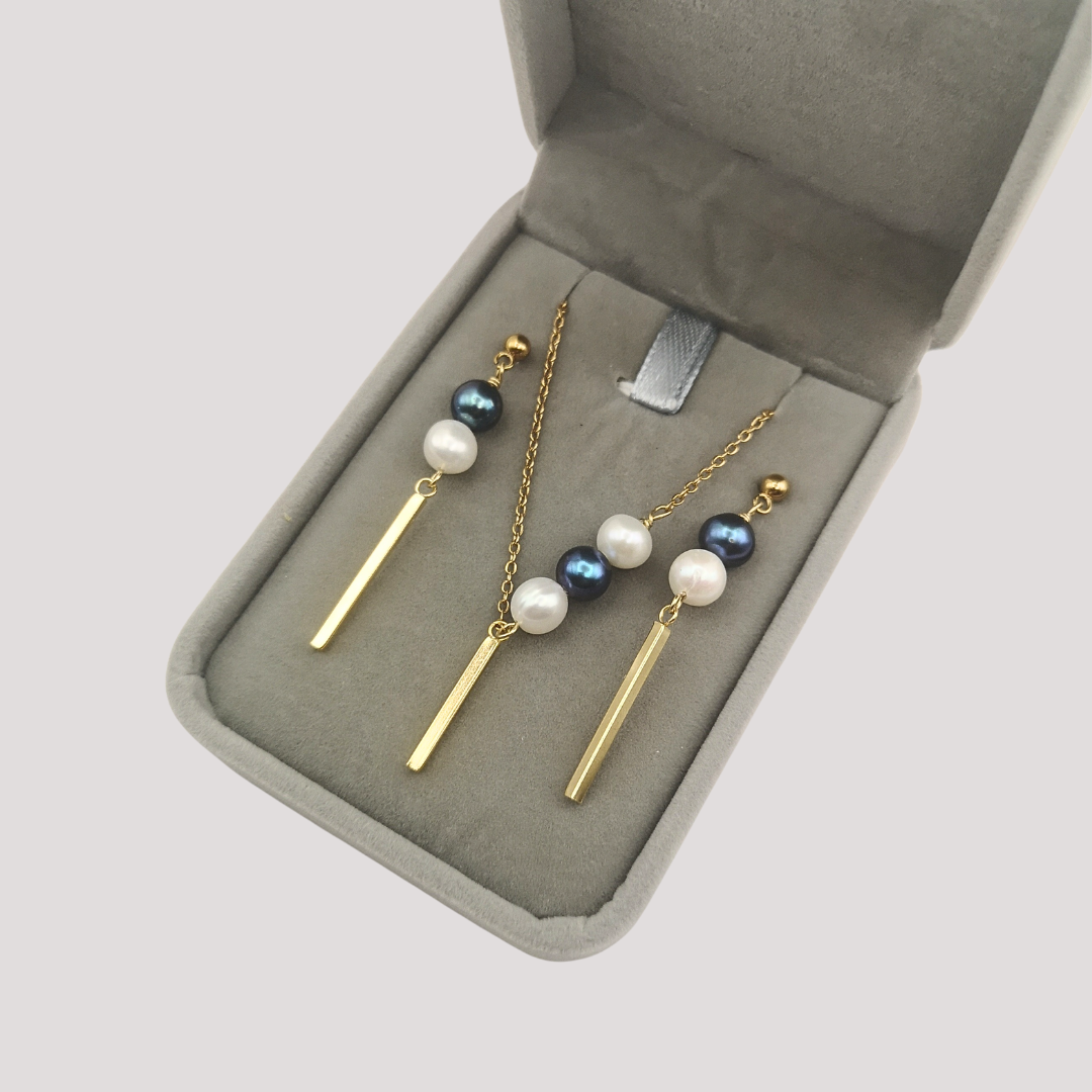 Set of gold and pearl earrings in a gray jewelry box on a light gray background