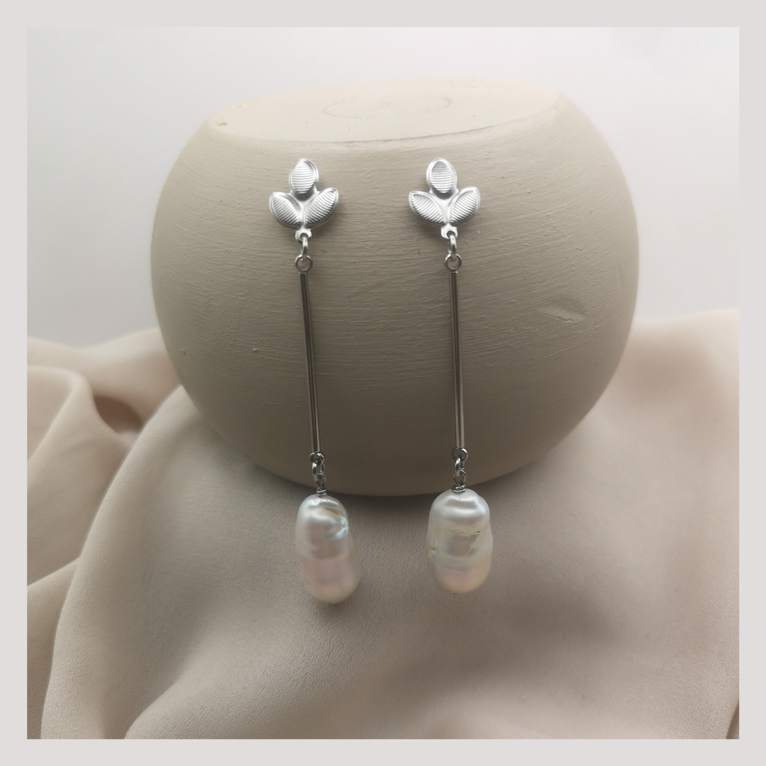 Stainless steel dangle baroque freshwater pearls hanging from a wooden block with a blush pink background
