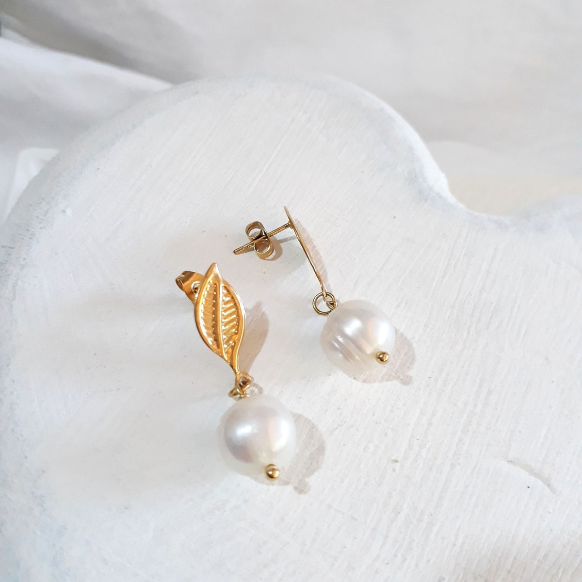 White freshwater pearl drops beneath gold-tone leaf-shaped ear studs with butterfly backs.
