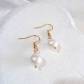 Near-round white freshwater pearl drop earrings on gold-tone shepherd ear hooks.