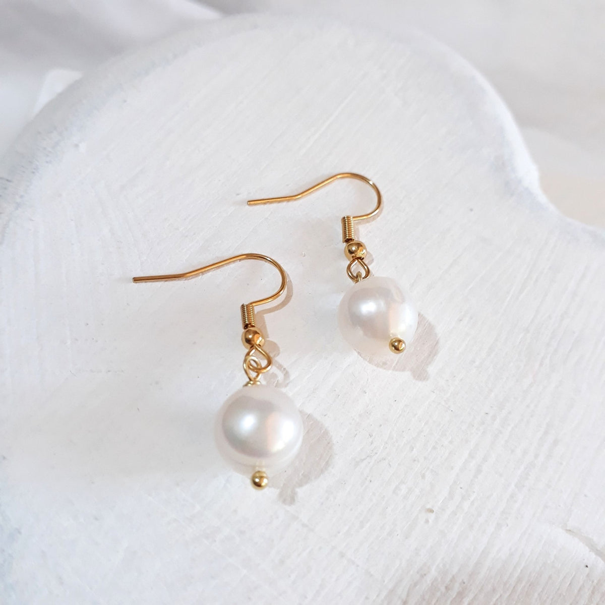 Near-round white freshwater pearl drop earrings on gold-tone shepherd ear hooks.