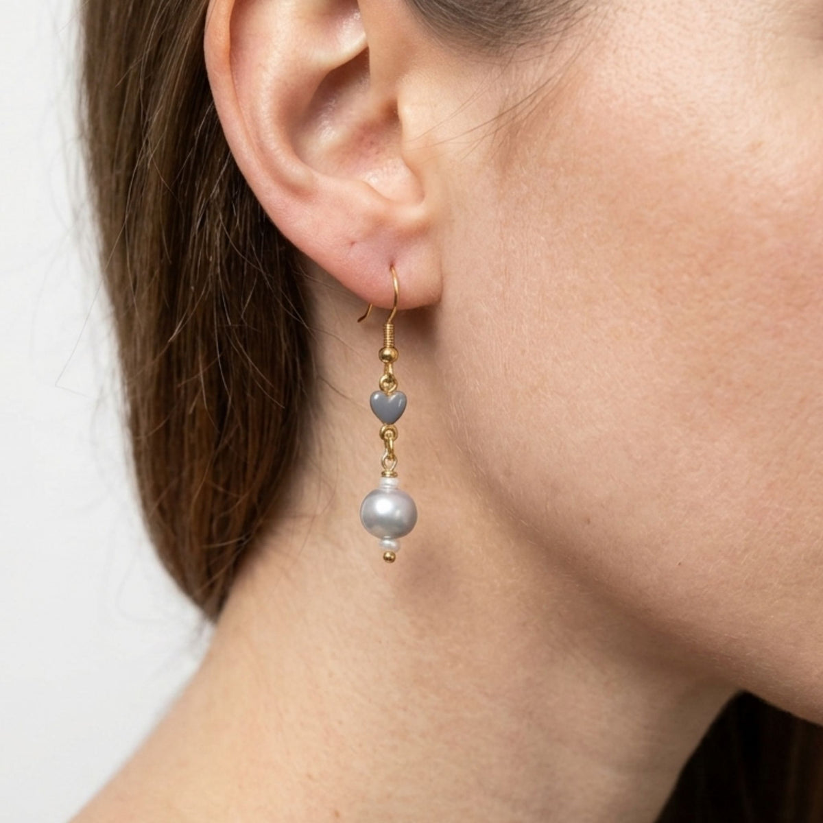 Awoman wearing a silver-grey freshwater pearl gold plated earring with a grey ceramic heart.