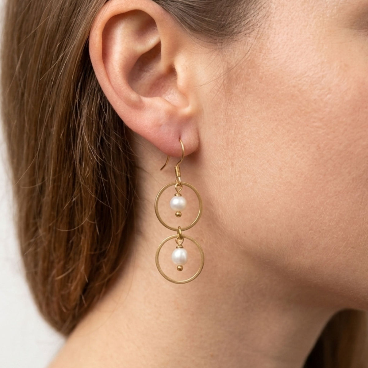 Close-up of a woman wearing a gold-plated double circle dangle earring with two white freshwater pearls.