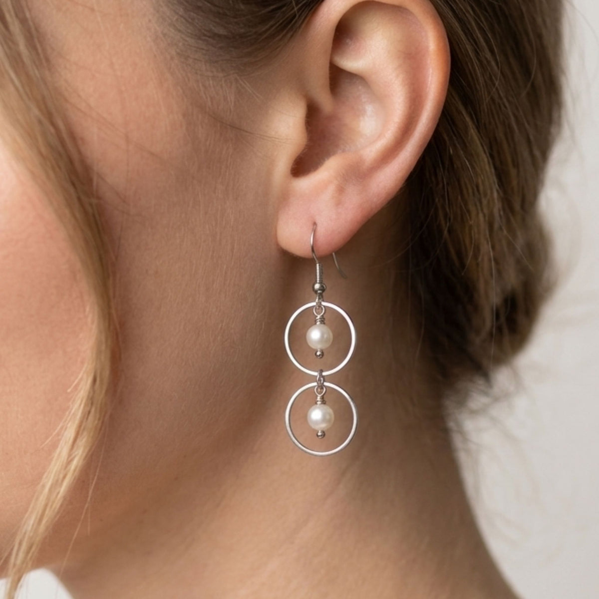 Close-up of a woman wearing a double circle stainless steel dangle earring with two white freshwater pearls.