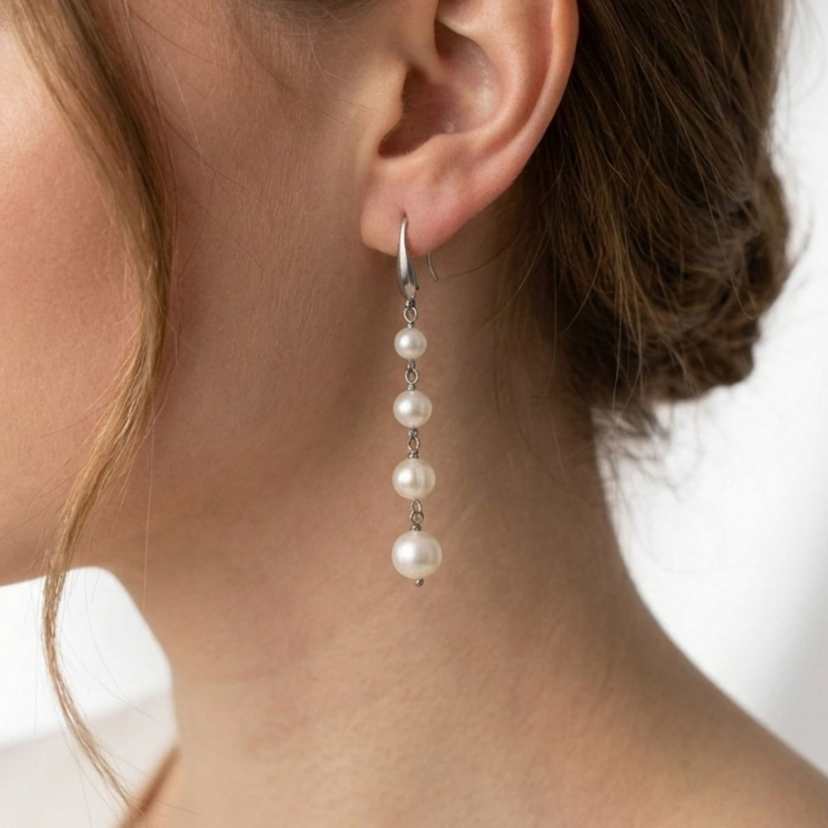 A woman wearing silver stainless steel white freshwater pearl cascade earrings.