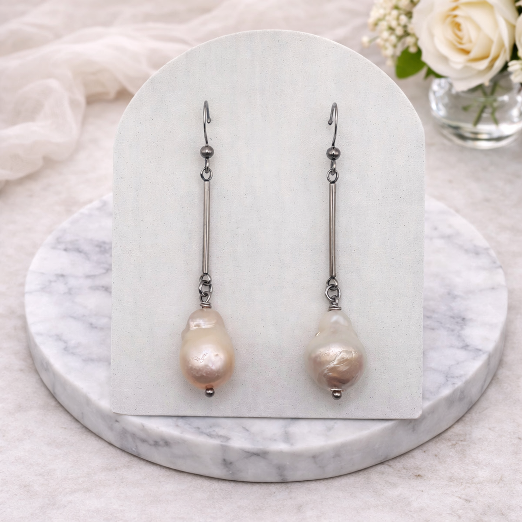 Pair of baroque pearl earrings on a white card with marble base and flowers in the background