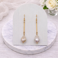 Pair of dangle baroque pearl earrings on a white card with a marble base