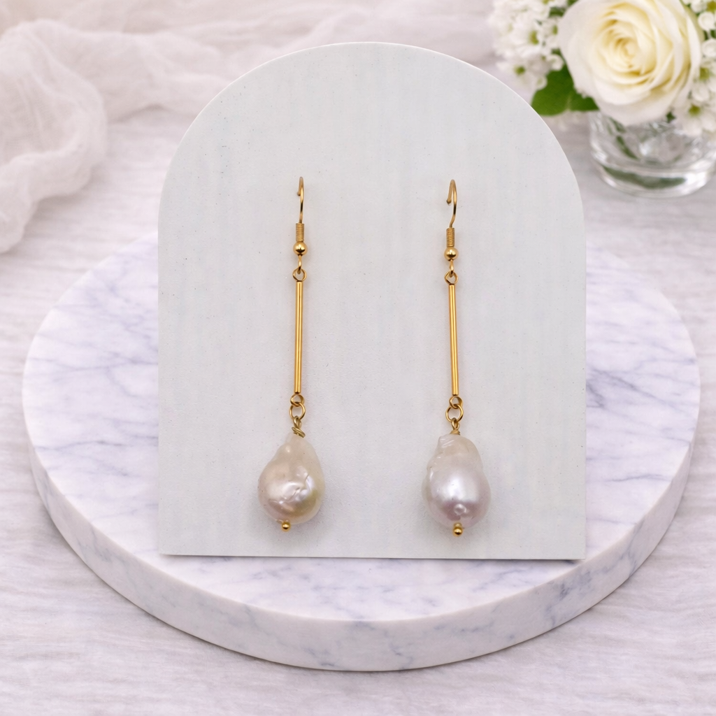 Pair of dangle baroque pearl earrings on a white card with a marble base