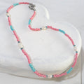 Beaded necklace with blue and pink beads and freshwater pearls lying on a white wooden surface