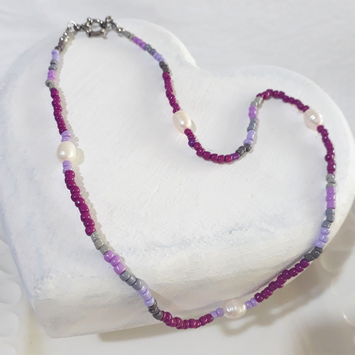 This handmade necklace pairs the luminous white of freshwater pearls with purple and grey glass beads