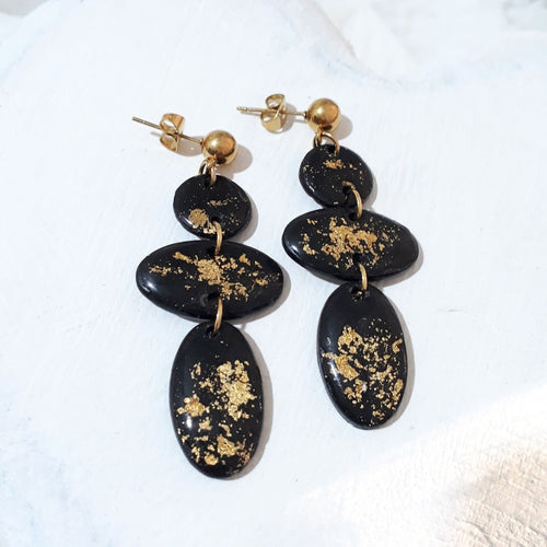 Black polymer clay earrings with gold-coloured flecks, three linked round and oval shapes, and gold-tone ball studs.