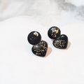 Glossy black polymer clay ear studs with rounded tops, heart-shaped lower pieces and scattered gold-coloured flecks.