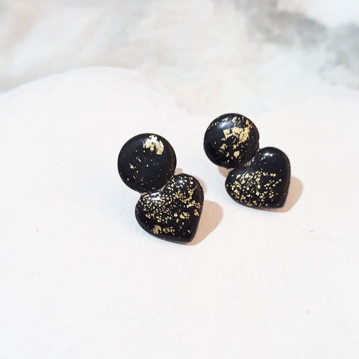 Glossy black polymer clay ear studs with rounded tops, heart-shaped lower pieces and scattered gold-coloured flecks.
