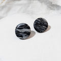 Glossy round black and white polymer clay stud earrings with flowing marbled stripes.