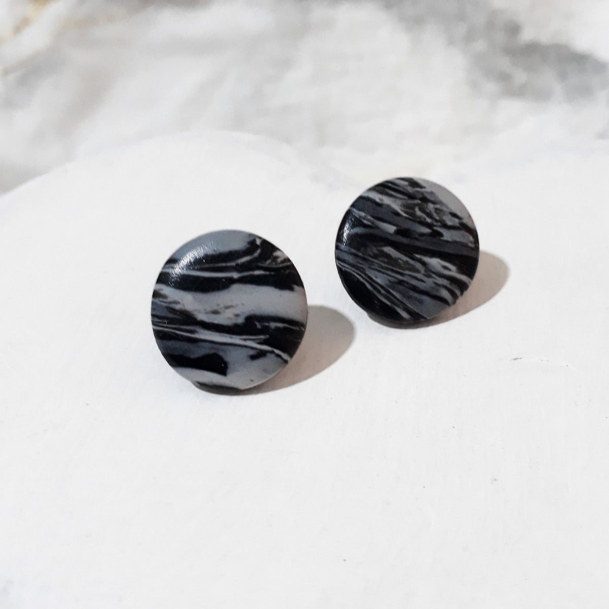 Glossy round black and white polymer clay stud earrings with flowing marbled stripes.