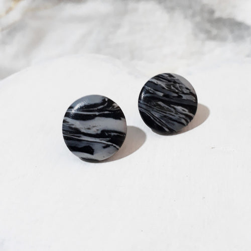 Glossy round black and white polymer clay stud earrings with flowing marbled stripes.