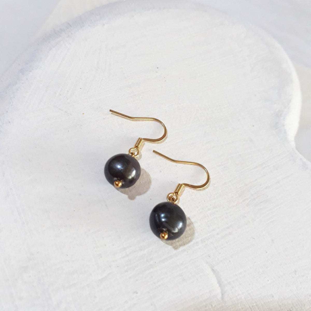 Black freshwater pearl drop earrings with gold-tone shepherd hooks and small gold-tone accents beneath each pearl.