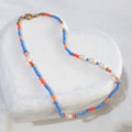 Blue and orange beaded necklace with freshwater pearls lying on a white wooden surface