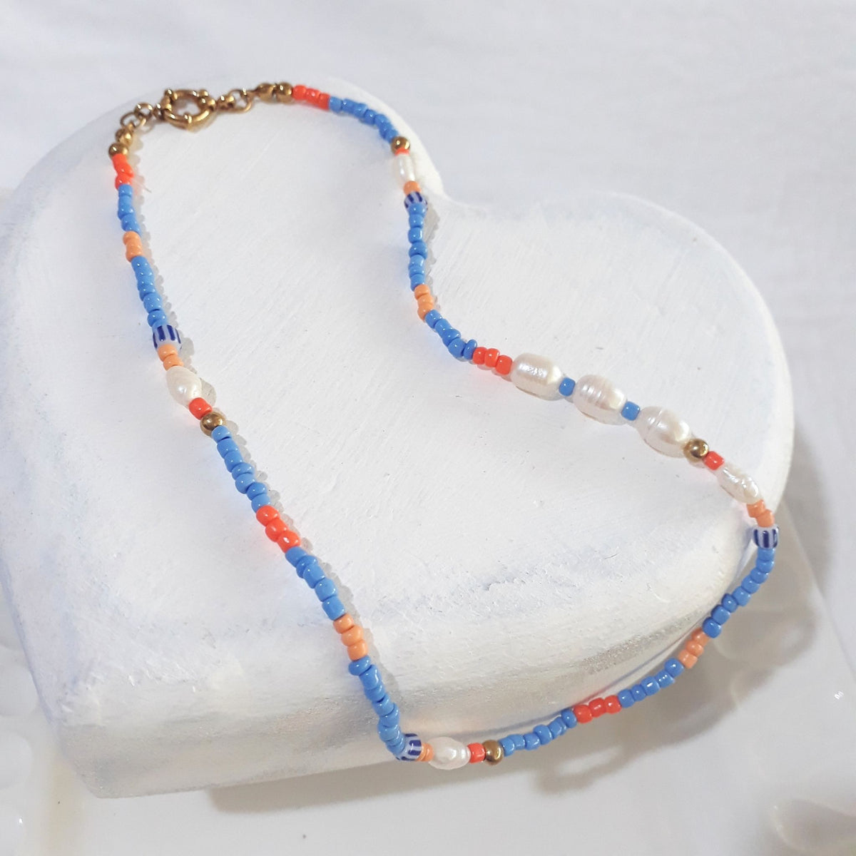 Blue and orange beaded necklace with freshwater pearls lying on a white wooden surface