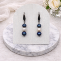 Pair of blue and white pearl earrings on a white card with a marble base