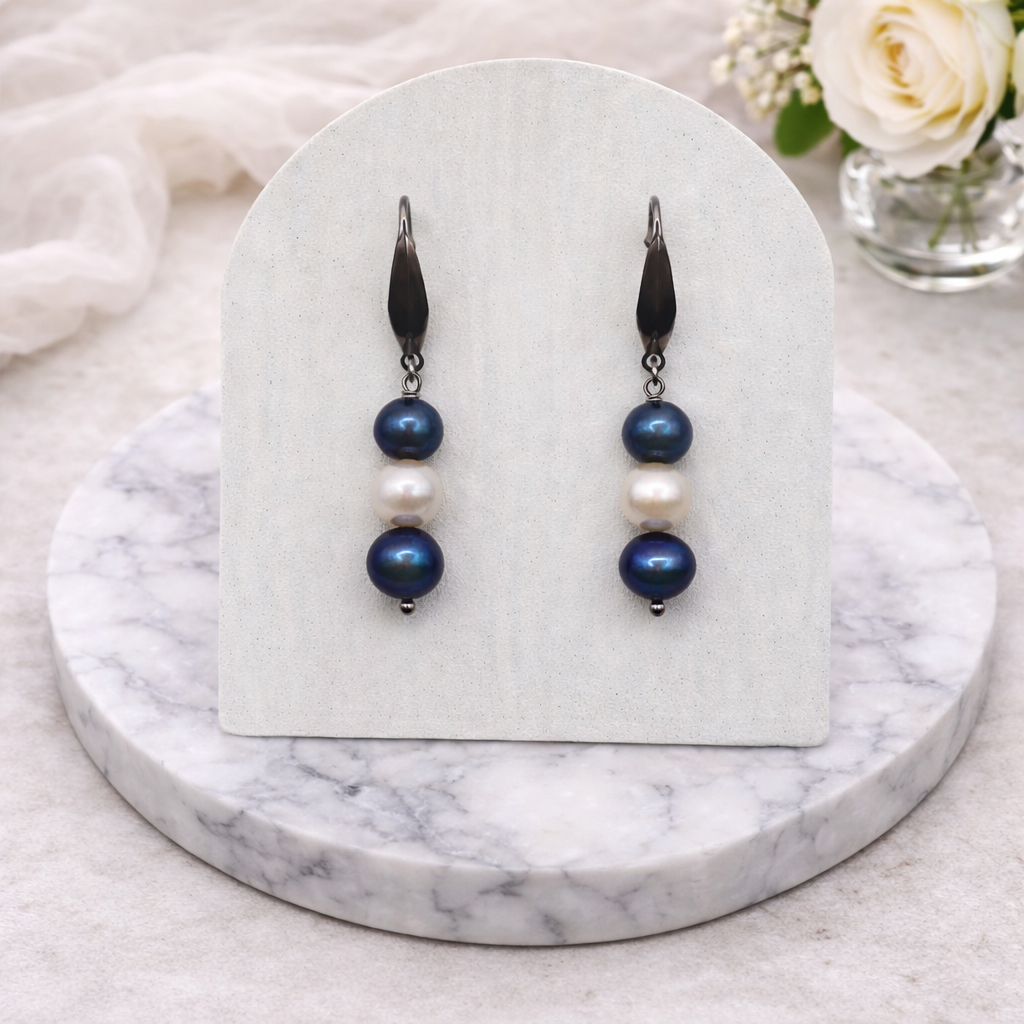 Pair of blue and white pearl earrings on a white card with a marble base