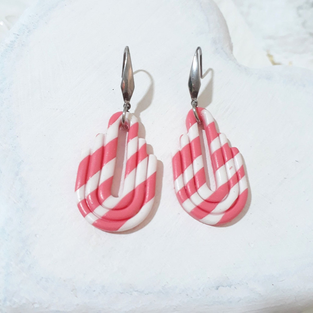 Bubblegum pink and white striped polymer clay earrings with stepped sides, rounded bases, elongated central cutouts and silver-tone ear hooks.