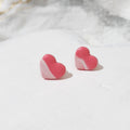 Bubblegum pink heart-shaped polymer clay stud earrings with sweeping white accents and gently shiny surfaces.