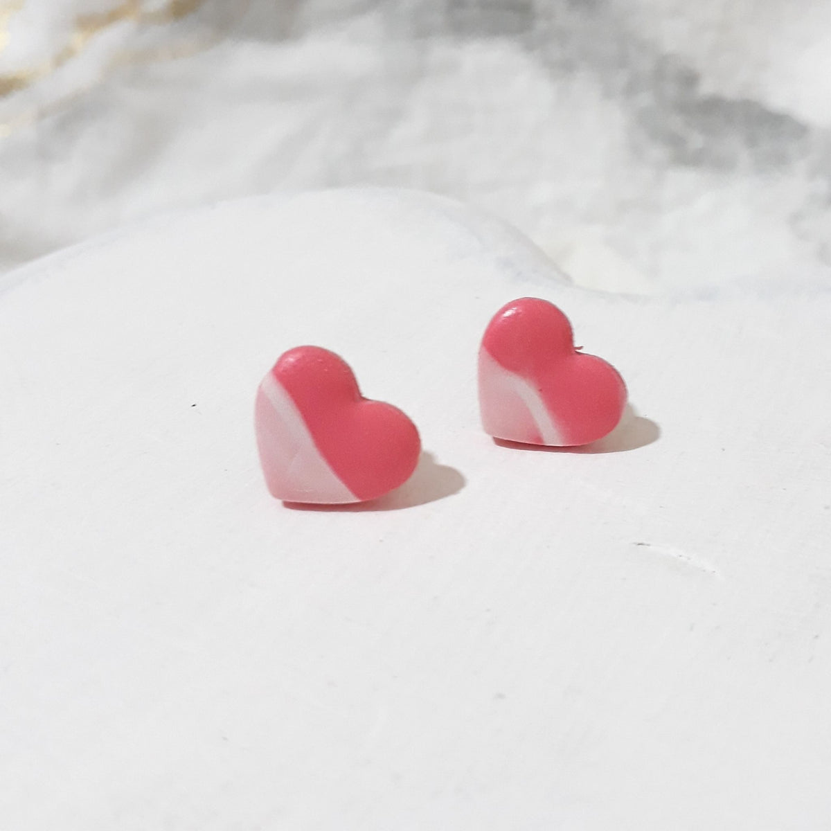 Bubblegum pink heart-shaped polymer clay stud earrings with sweeping white accents and gently shiny surfaces.