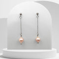 Pair of pink pearl earrings on a white stand with a light gray background