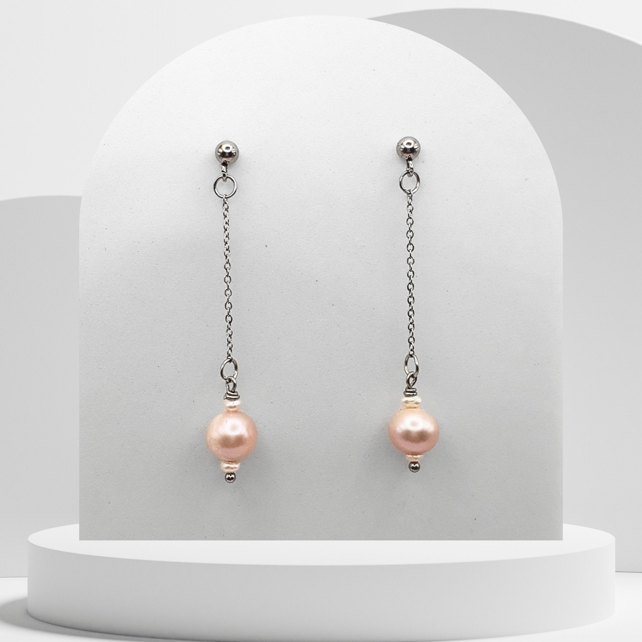 Pair of pink pearl earrings on a white stand with a light gray background