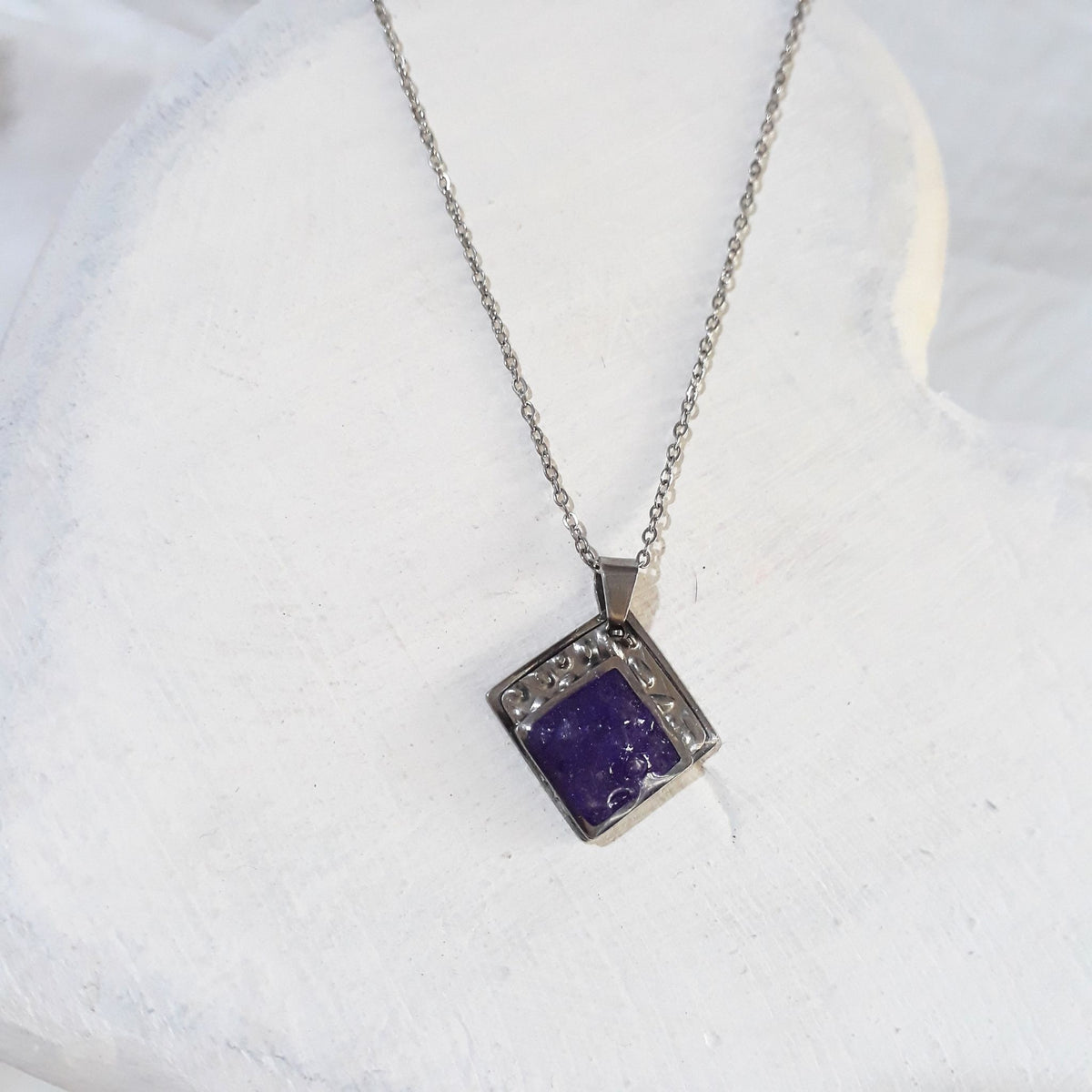 Diamond-shaped stainless steel pendant with purple crushed amethyst sealed in resin and a textured upper border on a silver-tone chain.