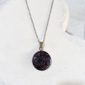 Round deep purple crushed amethyst pendant sealed in glossy resin in a silver-tone bezel on a stainless steel chain.