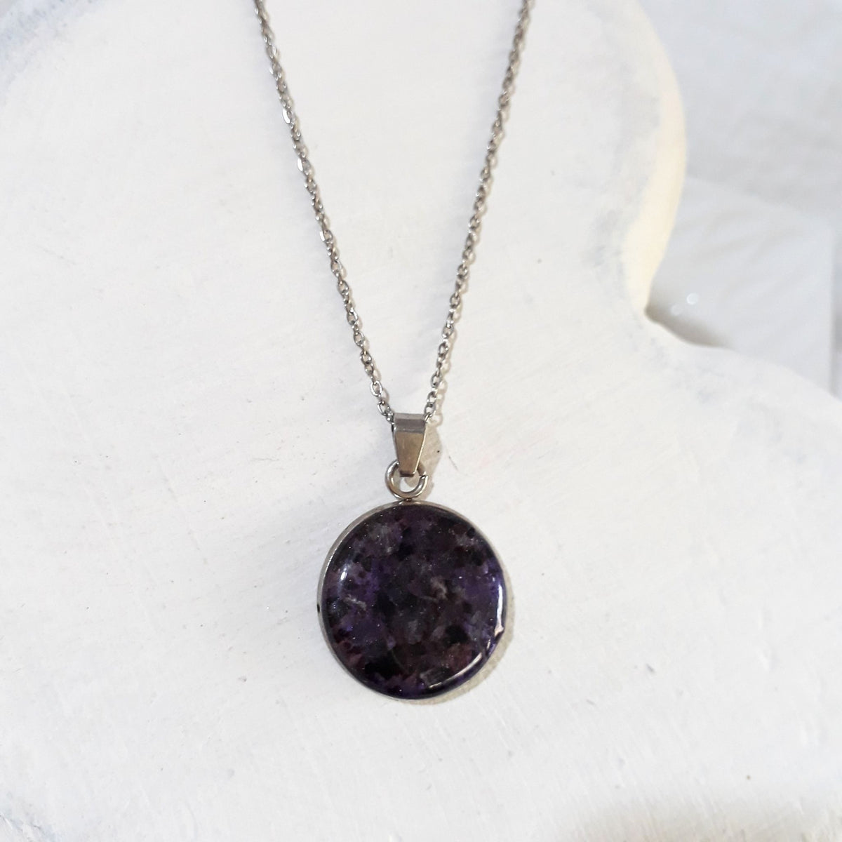 Round deep purple crushed amethyst pendant sealed in glossy resin in a silver-tone bezel on a stainless steel chain.