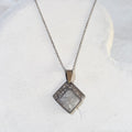 Diamond-shaped stainless steel pendant with crushed clear quartz sealed in resin and a textured upper border, hanging from a silver-tone chain.
