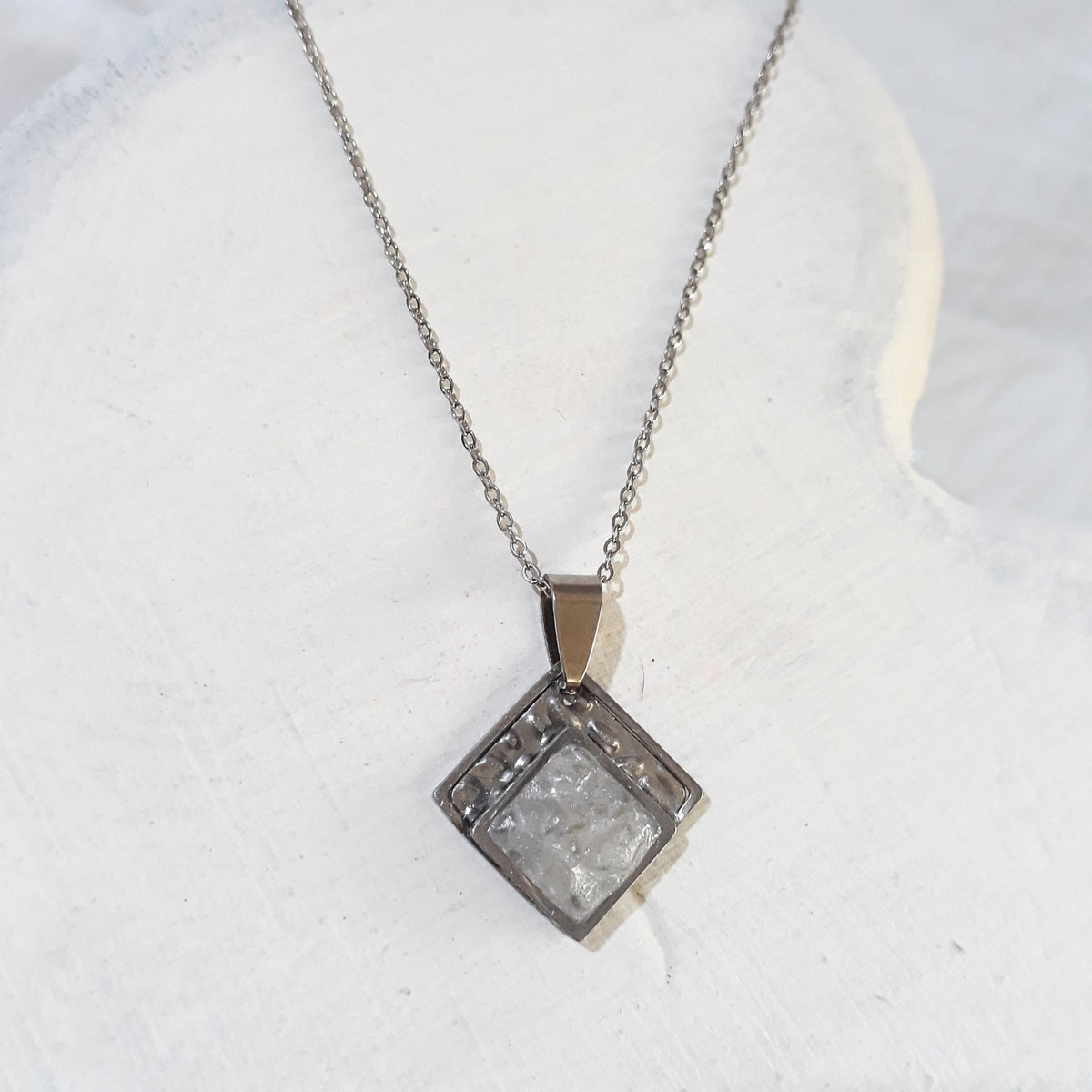 Diamond-shaped stainless steel pendant with crushed clear quartz sealed in resin and a textured upper border, hanging from a silver-tone chain.