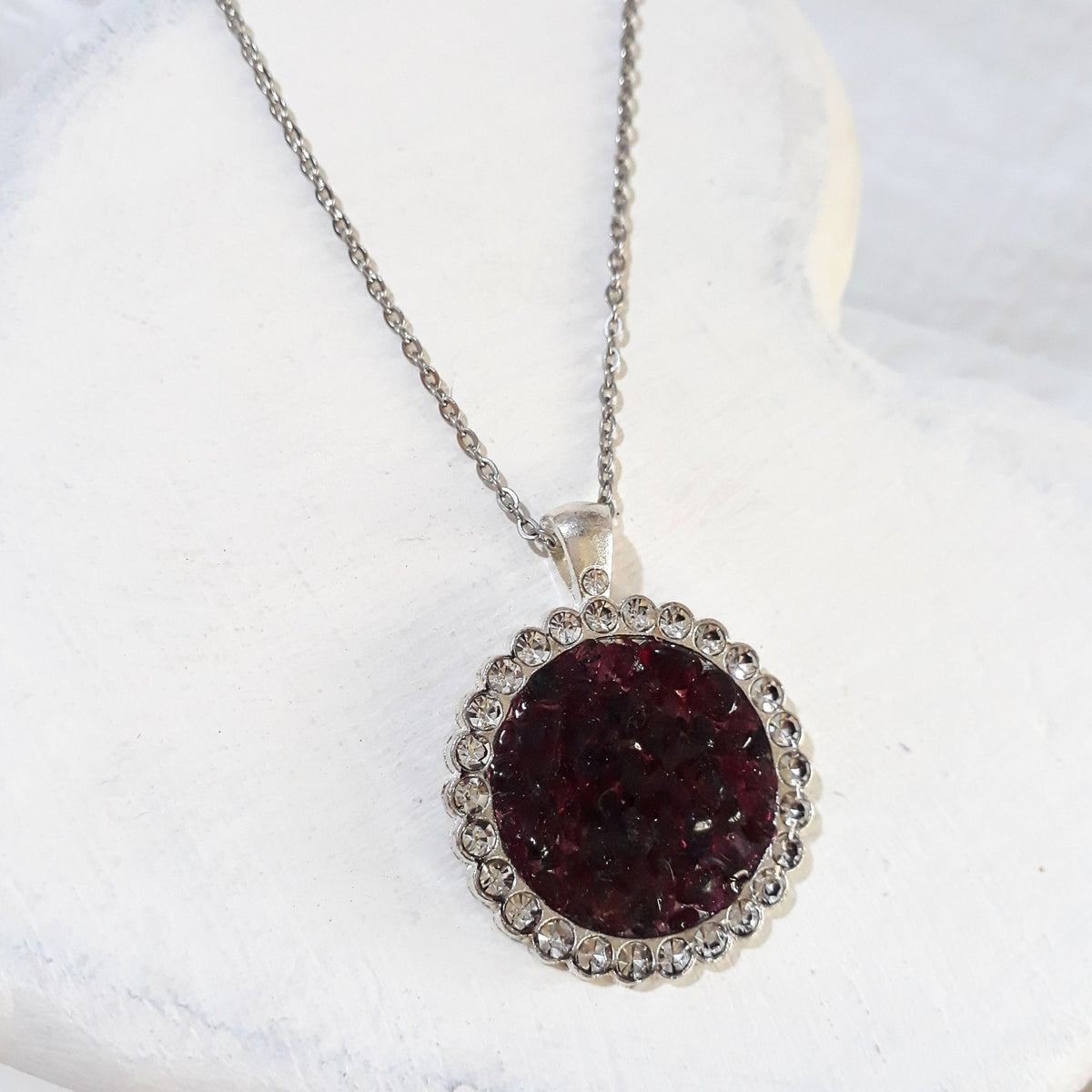 Round deep red crushed garnet pendant surrounded by clear rhinestones on a silver-tone stainless steel chain.