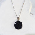 Dark crushed Starstone round pendant with tiny sparkling flecks in a silver-tone bezel on a stainless steel chain.