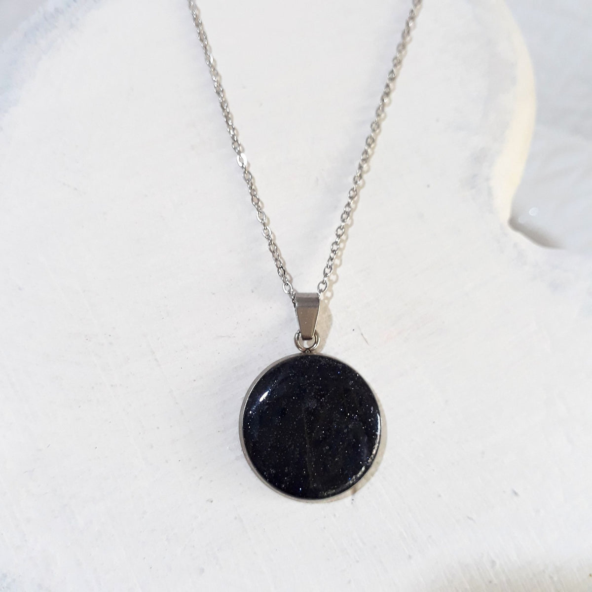 Dark crushed Starstone round pendant with tiny sparkling flecks in a silver-tone bezel on a stainless steel chain.