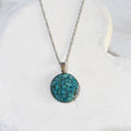 Round crushed turquoise pendant with blue-green pieces and darker markings in a stainless steel bezel on a silver-tone chain.