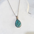 Teardrop pendant filled with blue-green crushed turquoise in a stainless steel frame on a silver-tone chain.