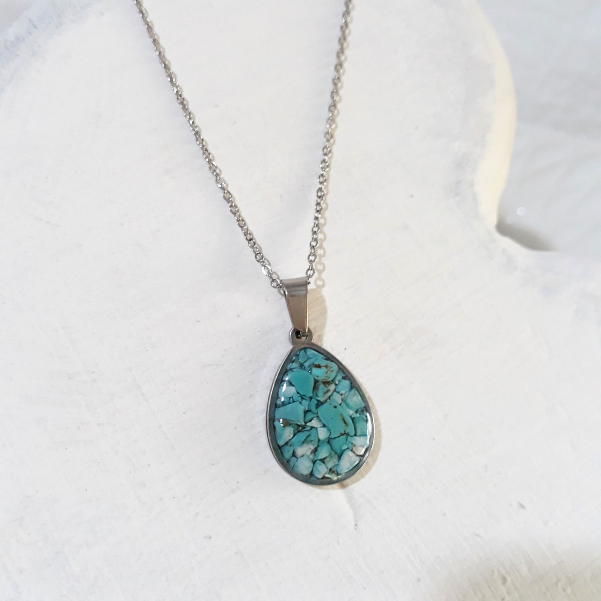 Teardrop pendant filled with blue-green crushed turquoise in a stainless steel frame on a silver-tone chain.