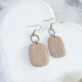 Warm beige polymer clay rounded rectangle earrings with a stippled texture, open silver-tone circular connectors and shepherd hooks.